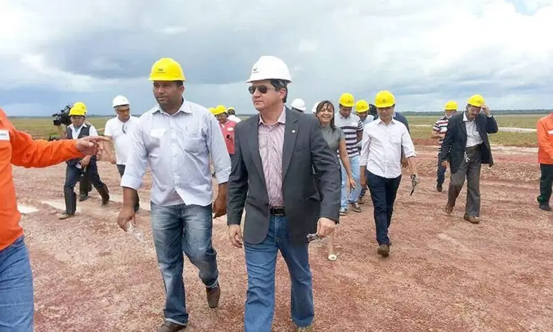 Deputados de capacete caminham sobre o terreno de terra vermelha da obra, em Bacabeira